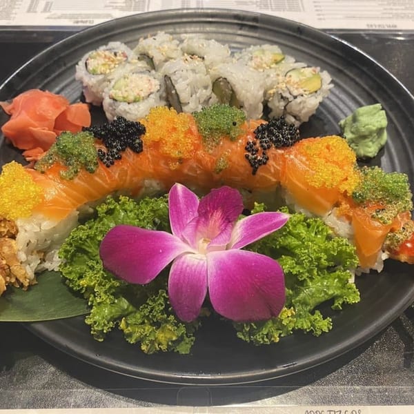 A black plate with various sushi rolls, including a dragon roll, garnished with a purple orchid.