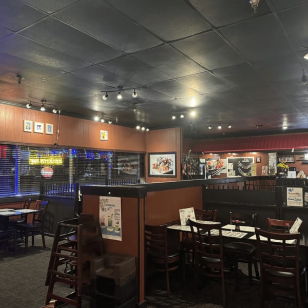 Interior of Koibito One Sushi & Teriyaki, featuring dining tables, chairs, and a window with neon signs.