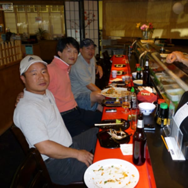 Three men sitting at a sushi bar with empty plates and drinks, enjoying a meal.