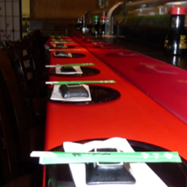 Sushi bar with red countertop, place settings, and dark chairs, ready for diners at Koibito One.
