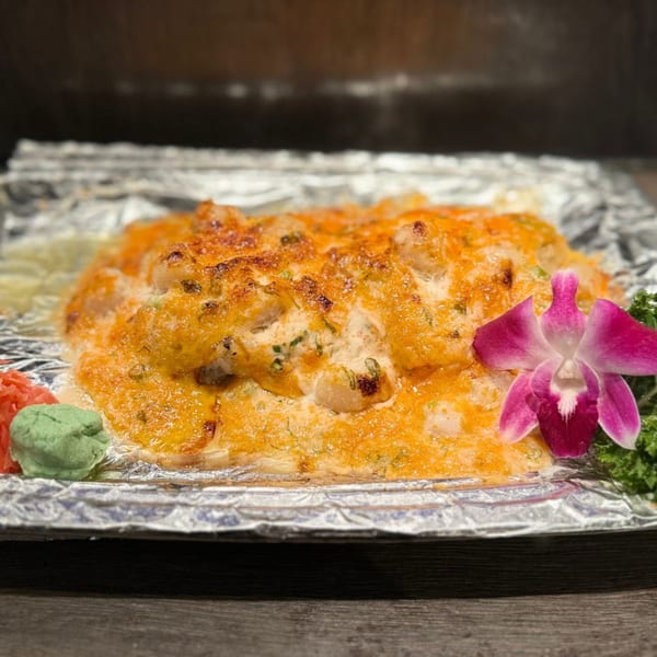 Baked Japanese dish with orange sauce, garnished with a pink orchid, wasabi, and ginger.