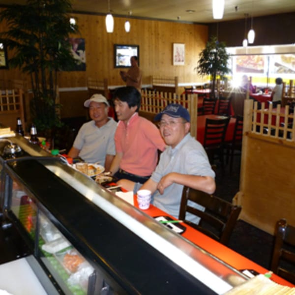 Three men seated at a sushi bar inside Koibito One Sushi & Teriyaki restaurant.