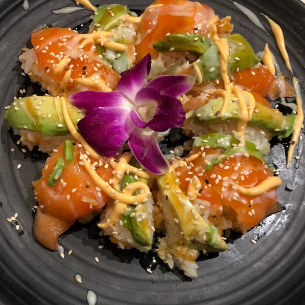 Koibito One Sushi & Teriyaki's salmon and avocado sushi rolls, drizzled with sauces and garnished with a purple orchid.