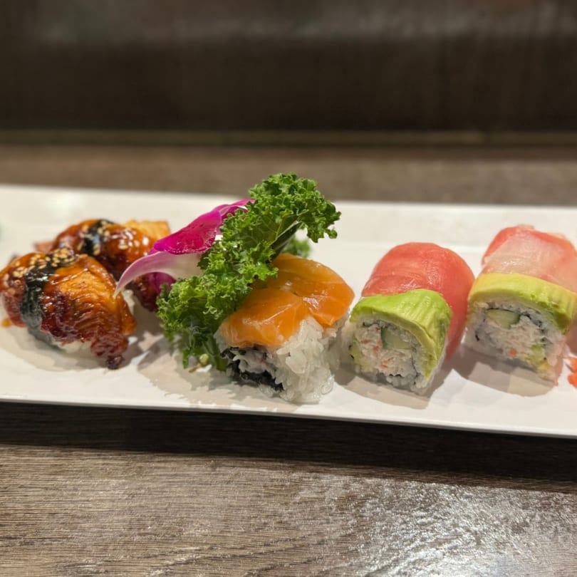 Assortment of Koibito One Sushi & Teriyaki rolls with salmon, tuna, avocado, and eel on a white plate.