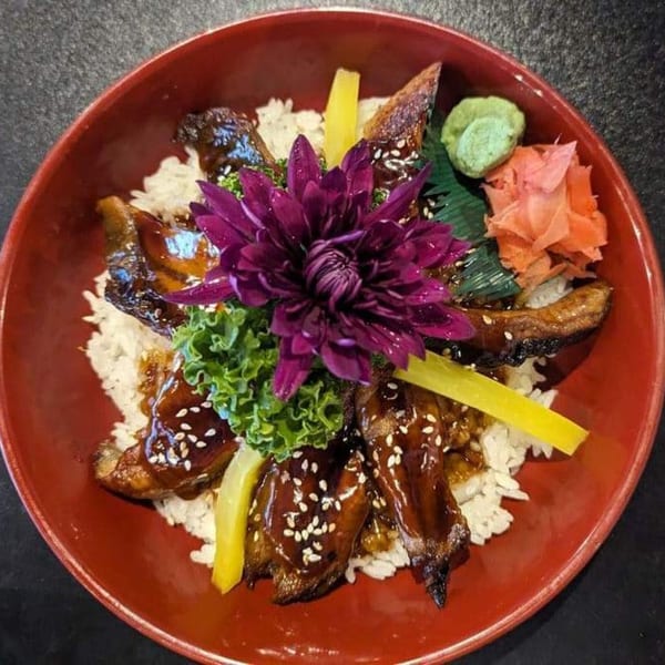 Koibito One Sushi & Teriyaki's unagi donburi with eel, rice, pickled ginger, wasabi, and a purple flower.