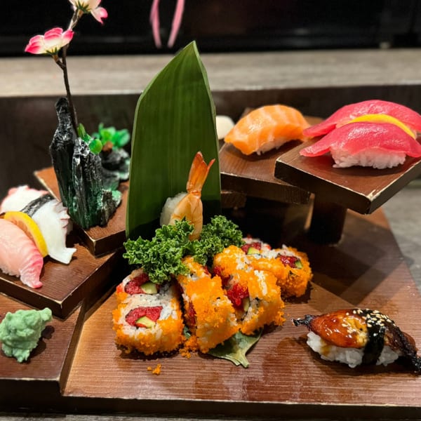 A Japanese sushi and sashimi platter with various rolls, nigiri, and wasabi on a wooden board.