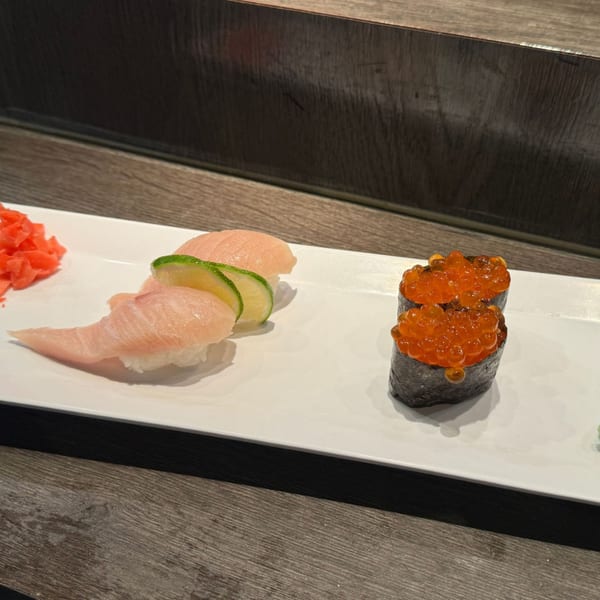 A white plate with two pieces of salmon nigiri, two pieces of salmon roe gunkan, and pickled ginger.