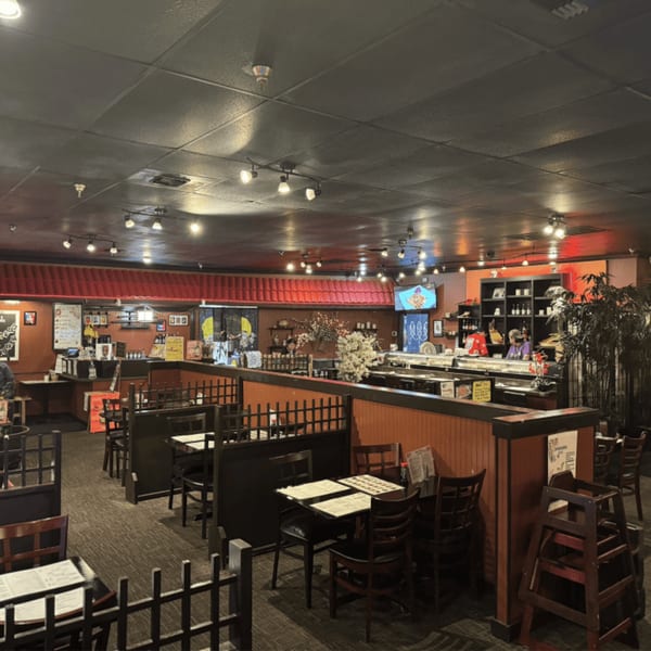 Interior of Koibito One Sushi & Teriyaki, showing dining tables, a sushi bar, and red accents.