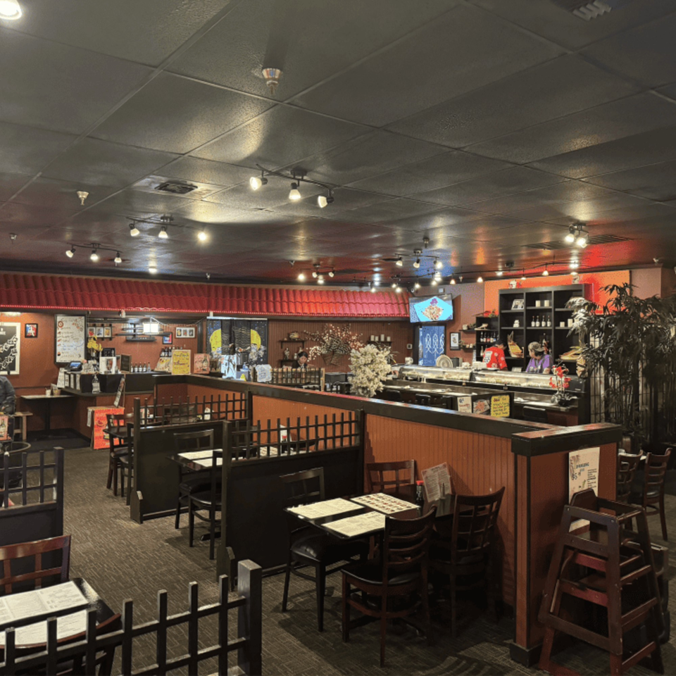 Interior of Koibito One Sushi & Teriyaki, showing dining tables, a sushi bar, and red accents.