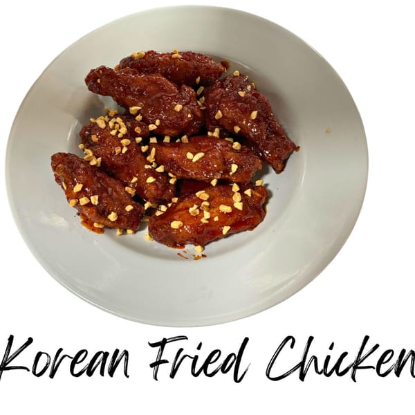 A white plate holds several pieces of Korean fried chicken, glazed and topped with chopped peanuts.