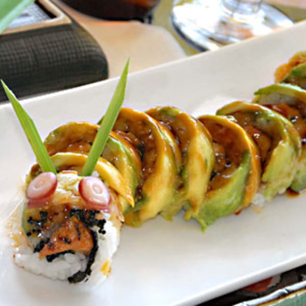 Caterpillar sushi roll with avocado slices, eel sauce, and red roe eyes on a white plate.