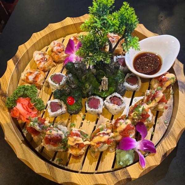 A large wooden platter with various sushi rolls, ginger, wasabi, and a decorative bonsai tree.