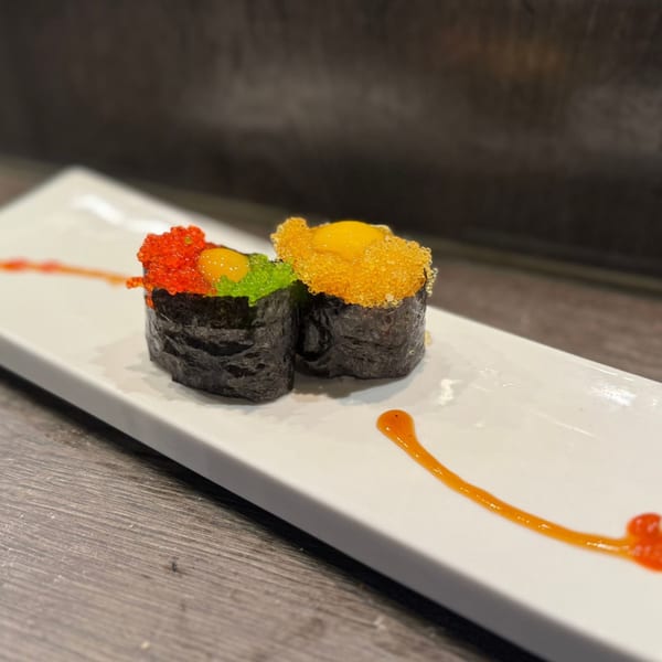 Two colorful Koibito One sushi rolls with quail egg, tobiko, and sauce on a white plate.