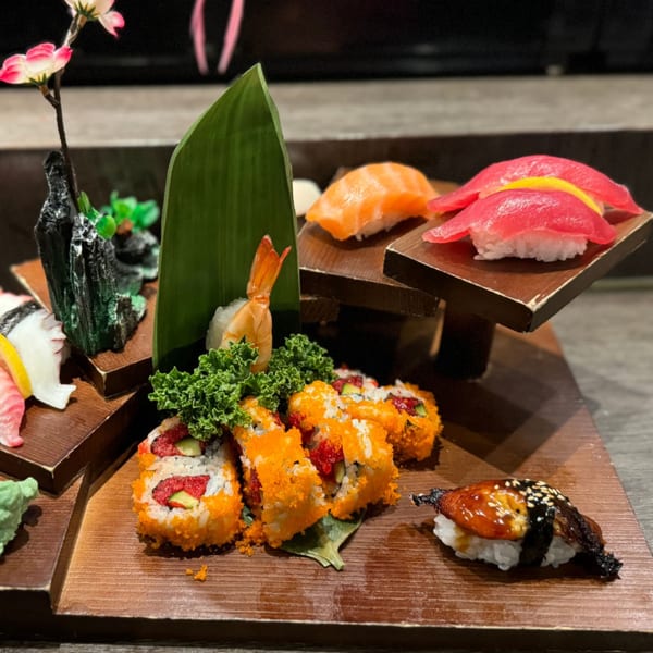 Assorted sushi and sashimi, including tuna, salmon, shrimp, and California rolls, on wooden serving boards.