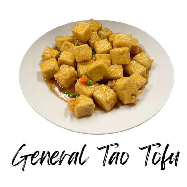 A white plate filled with golden-brown General Tso Tofu cubes, garnished with peas and carrots.