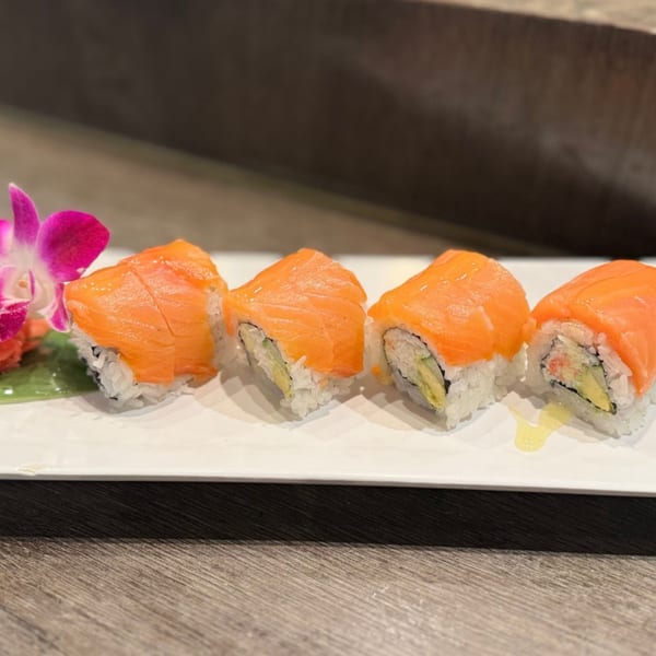 Four pieces of salmon sushi with avocado and crab, garnished with a pink orchid.