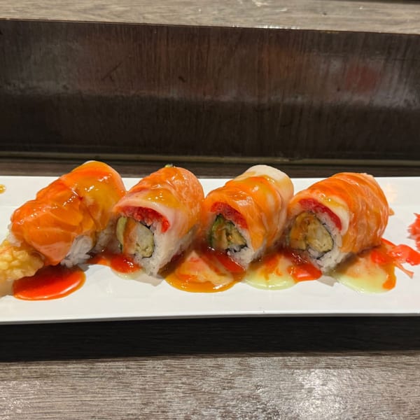 Four sushi rolls with salmon and white fish on top, drizzled with orange and yellow sauces.