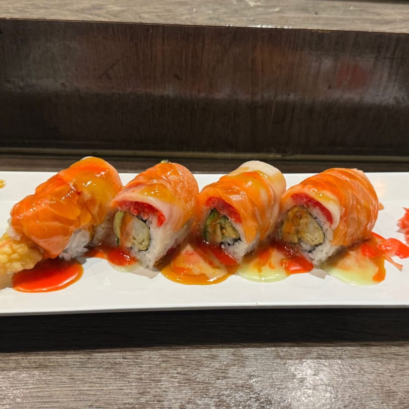 Four sushi rolls with salmon and white fish on top, drizzled with orange and yellow sauces.