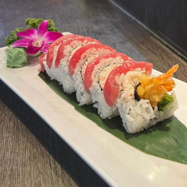 A Koibito One Sushi & Teriyaki roll with tuna, shrimp tempura, and crab, garnished with a purple orchid.