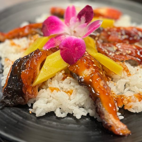Koibito One Sushi & Teriyaki's unagi donburi with grilled eel, yellow pickled daikon, and a pink orchid.