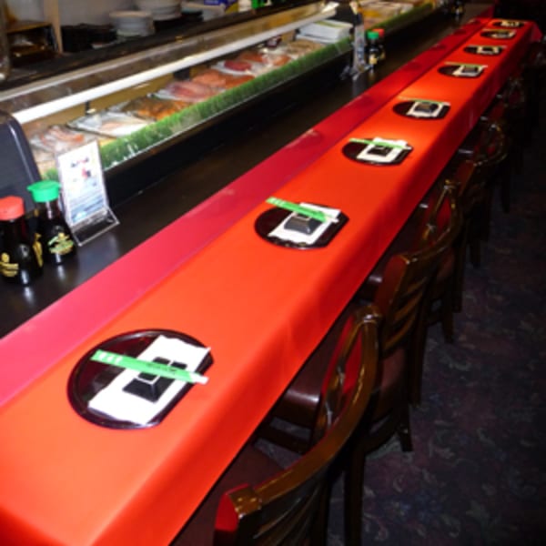 A long sushi bar with a red conveyor belt, set with plates and chopsticks, and a display of fresh fish.
