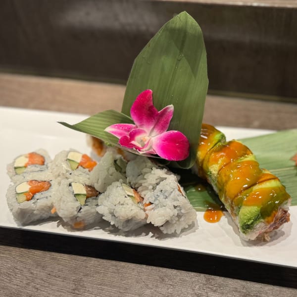 Two types of sushi rolls on a white plate, garnished with a green leaf and pink orchid.