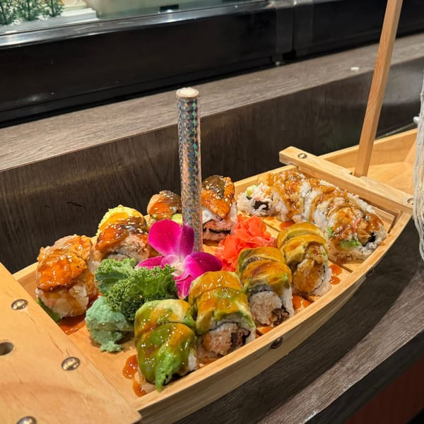 A wooden boat filled with various sushi rolls, garnished with ginger, wasabi, and a pink orchid.