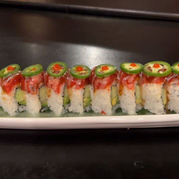A row of Koibito One sushi rolls with avocado, red topping, and jalapeño slices on a white plate.