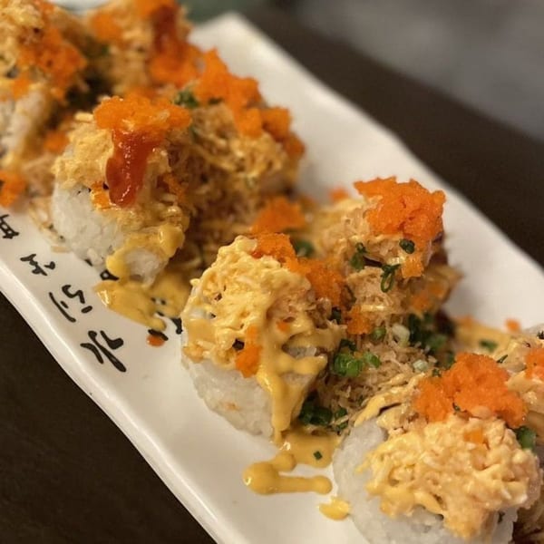 Koibito One Sushi & Teriyaki's sushi rolls topped with orange roe, sauce, and green onions.