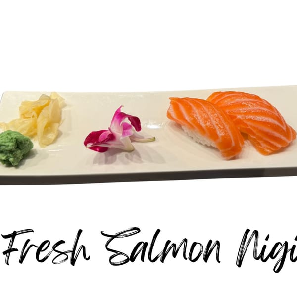 Two pieces of salmon nigiri with wasabi, pickled ginger, and an orchid on a white plate.