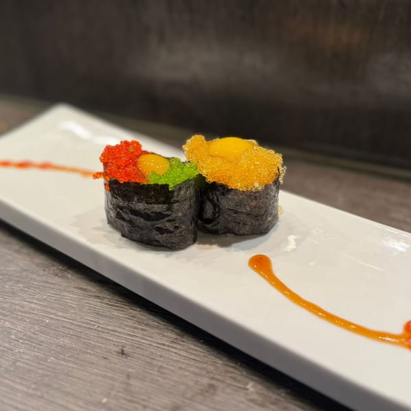Two colorful Koibito One sushi rolls with bright orange and green roe on a white plate.