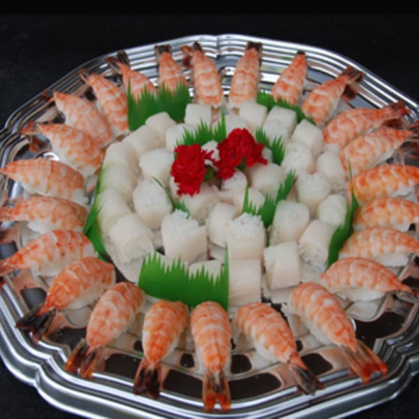 A silver platter filled with shrimp nigiri and white sushi rolls, garnished with red flowers.