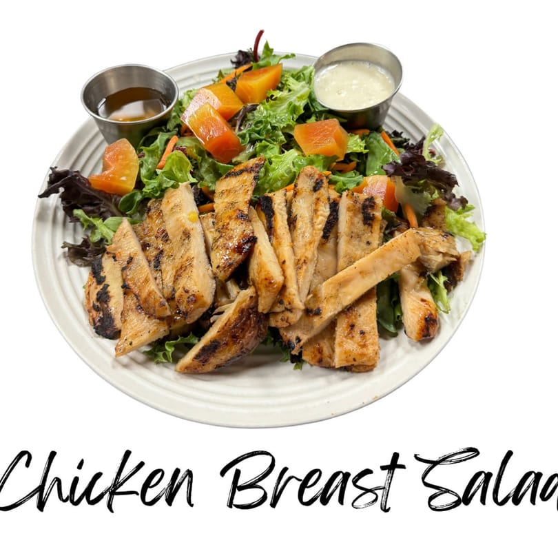 Grilled chicken breast salad with mixed greens, papaya, and two dressing cups on a white plate.
