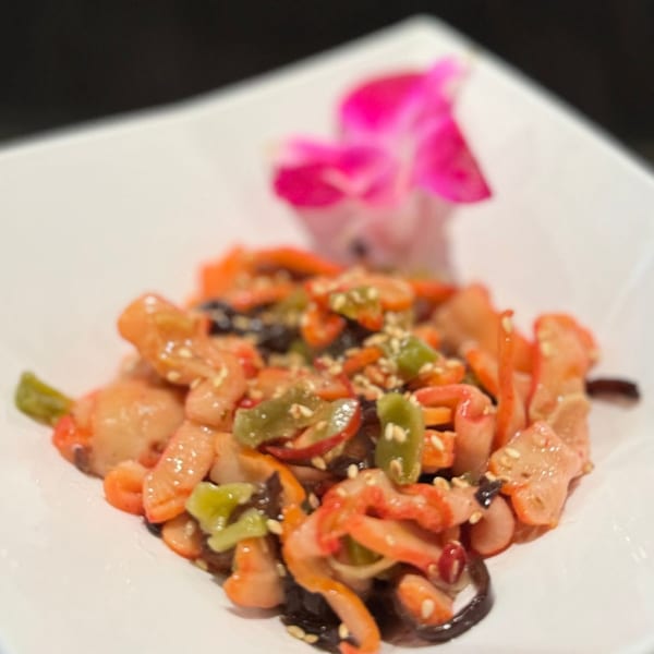 A Japanese salad with seafood, green peppers, and sesame seeds, garnished with a pink orchid.