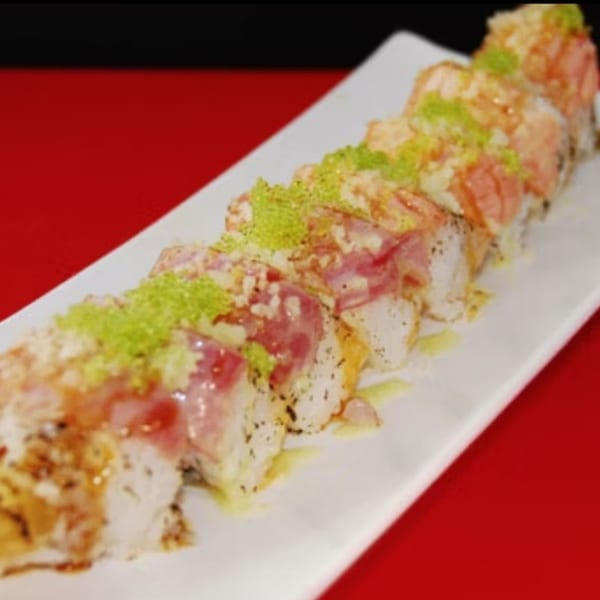 A long white plate holds a row of Koibito One sushi rolls topped with tuna and green roe.
